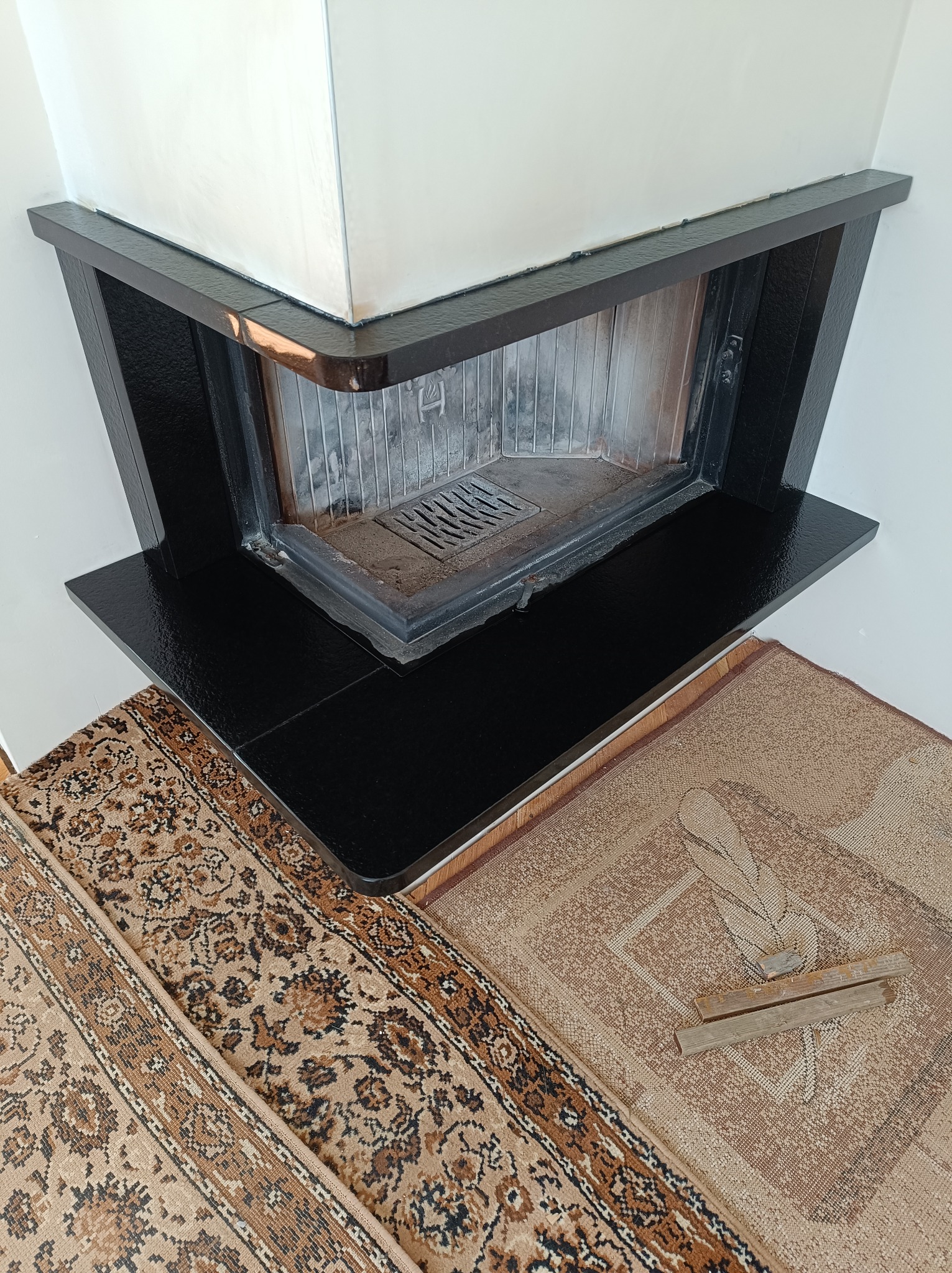 Wykończenie kominka czarnym, błyszczącym kamieniem, widok z góry, fragment dywanu w tle.