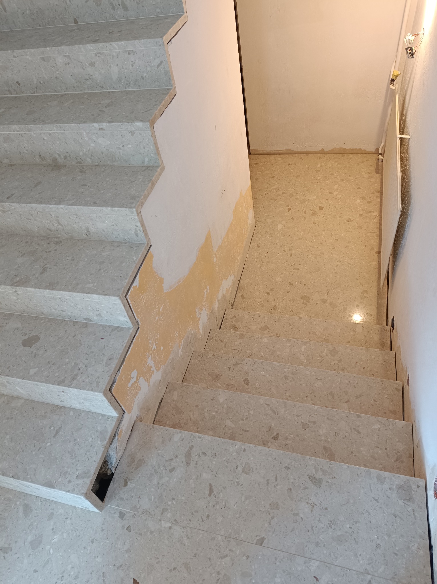 Wykończone schody wewnętrzne z lastryko w trakcie prac wykończeniowych ściany, widoczny fragment podłogi z tego samego materiału.