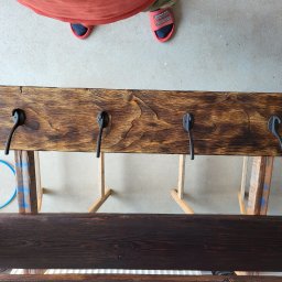 Usługi ogólnobudowlane Artur Klecha - Wieszak ścienny z ciemnego drewna z czterema czarnymi haczykami, przymocowany do prowizorycznego stojaka podczas prac wykończeniowych, widok z góry.