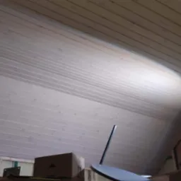 Drewniane deski sufitowe z widocznym oświetleniem punktowym, kartonowe pudło i inne przedmioty w tle.