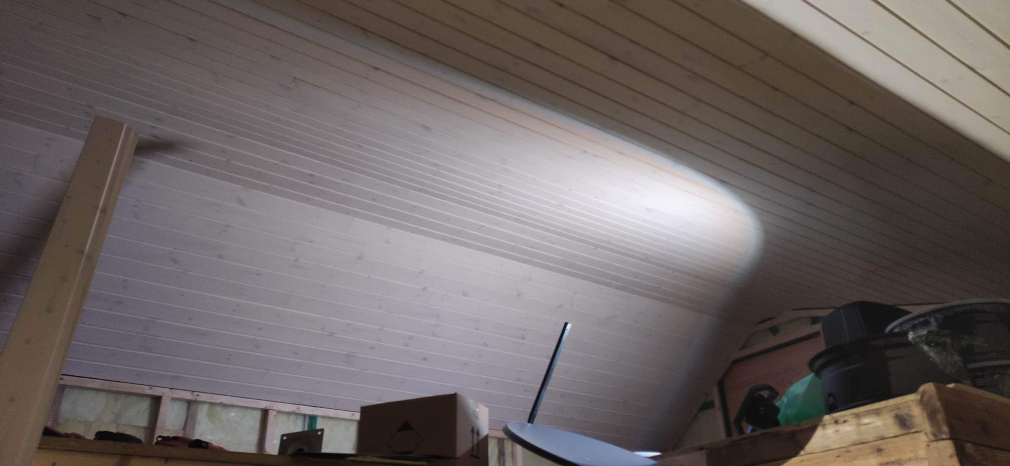 Drewniane deski sufitowe z widocznym oświetleniem punktowym, kartonowe pudło i inne przedmioty w tle.