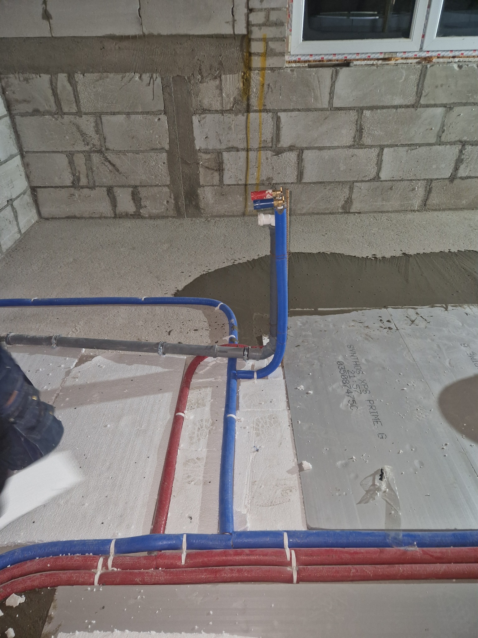 Surowe wnętrze w trakcie prac instalacyjnych: widoczne nieotynkowane ściany z betonu komórkowego, podłoże z płyt styropianowych oraz rozprowadzone rury instalacji wodnej i grzewczej, częściowo...