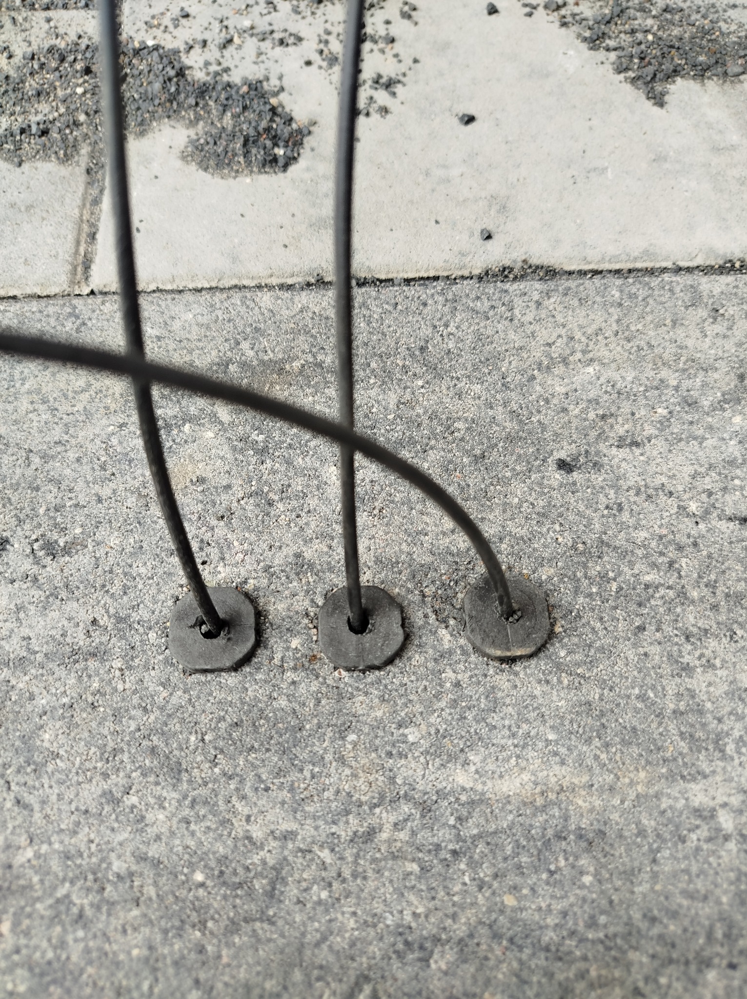 Przygotowane otwory z przewodami na szarym chodniku, prawdopodobnie pod montaż oświetlenia w przestrzeni miejskiej, z bliska.