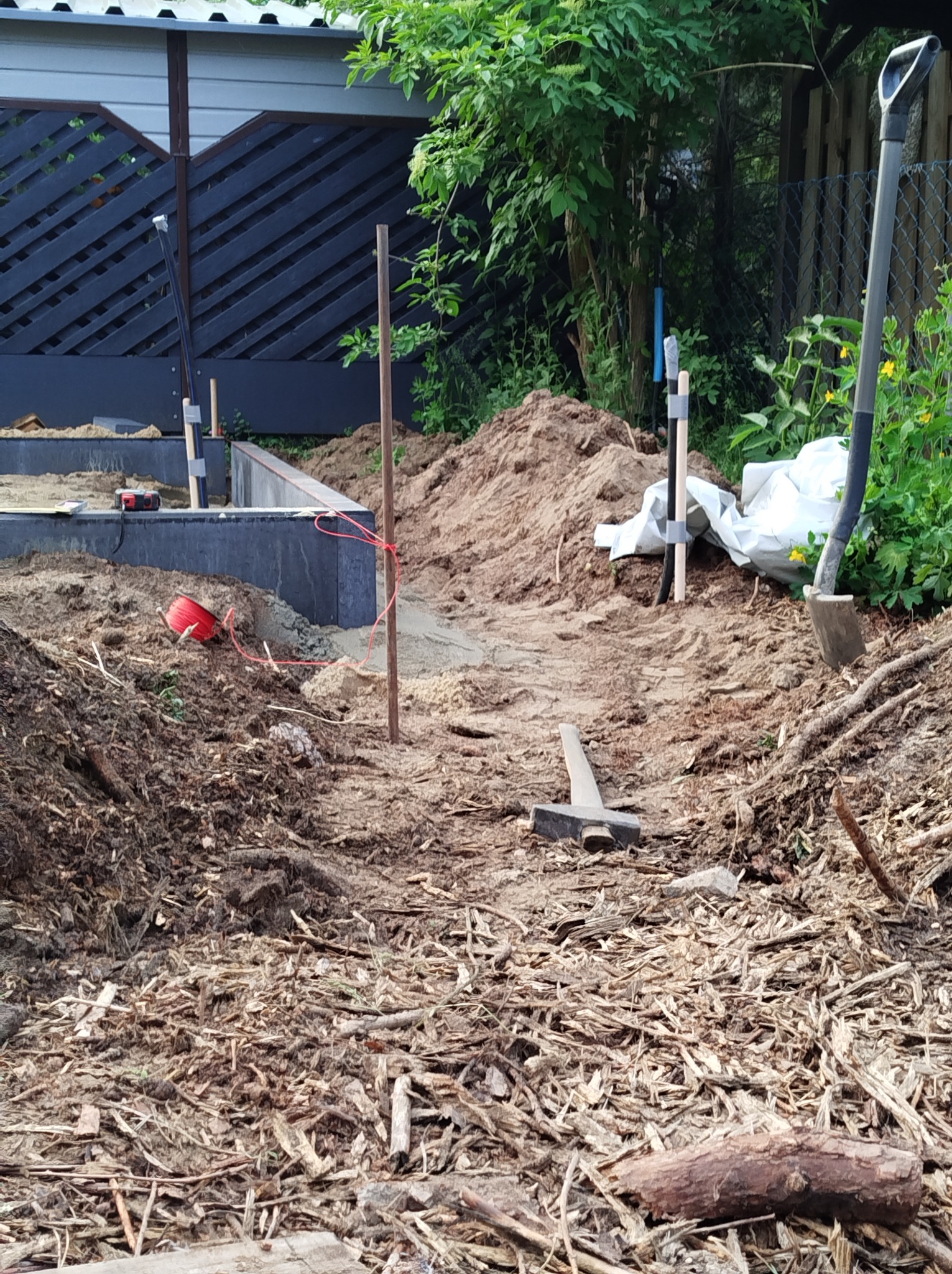 Przygotowanie terenu pod budowę, widoczne narzędzia, ziemia, drewniane podpory i częściowo wylany fundament z szarych betonowych bloków.