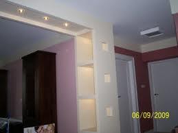 Wnętrze po remoncie: biała ściana z wnękami podświetlonymi kwadratowymi lampkami, widok na sąsiednie pomieszczenie z ciemnymi meblami i różową ścianą.