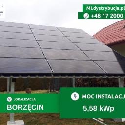 Instalacja paneli słonecznych na konstrukcji wsporczej, widoczny dach domu w tle, zieleń i logo firmy w górnym rogu.