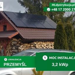 Dom jednorodzinny z zainstalowanymi panelami słonecznymi na dachu; widoczny stos drewna pod okapem i zaparkowany jasny samochód osobowy. Na zdjęciu nakładka graficzna z danymi kontaktowymi...