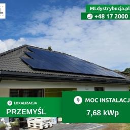 Panele słoneczne na dachu domu jednorodzinnego, widok z dołu, błękitne niebo w tle, logo firmy w prawym górnym rogu.