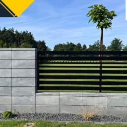 Firma Handlowa PROSPER SYLWIA KUŁAGA-CZERNECKA - Nowoczesne ogrodzenie z szarej kostki betonowej z czarnymi, poziomymi przęsłami, otoczone ozdobnym żwirem i zielenią, z drzewem w tle i logo firmy Prosper w prawym górnym rogu.