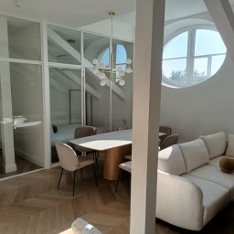 MIPAS-BUD VOLODYMYR PASHCHUK - Nowoczesne wnętrze: jasny salon z parkietem w jodełkę, szklane ściany działowe, okrągłe okno na poddaszu i designerska lampa nad stołem. Minimalistyczny wystrój.