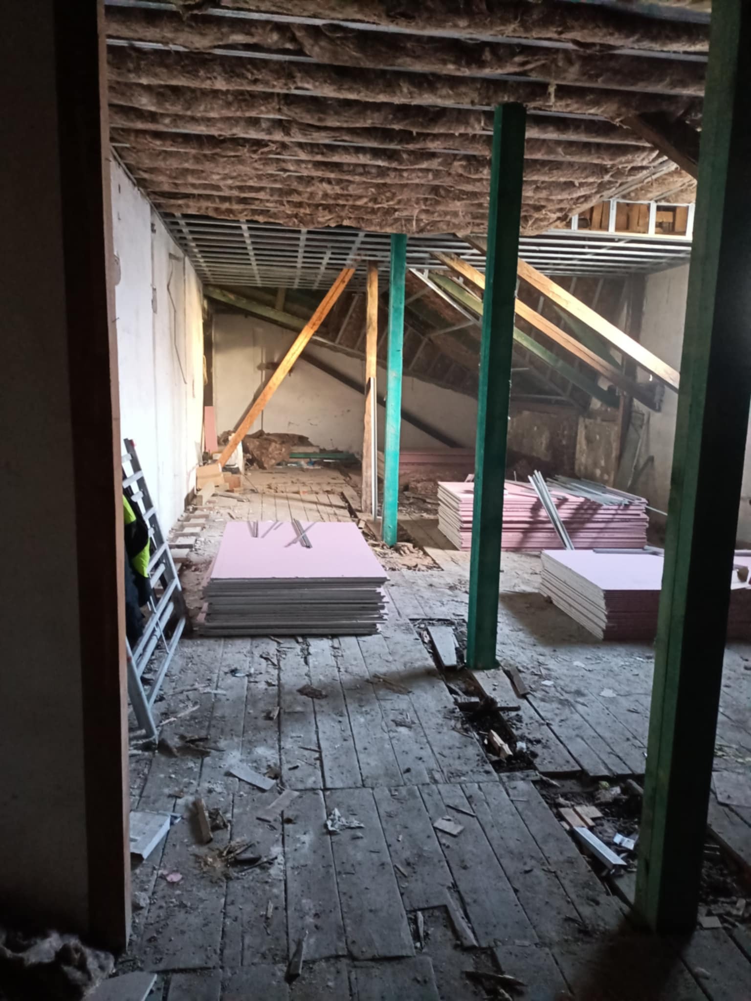 Poddasze w trakcie ocieplania, widoczne płyty izolacyjne, drewniane belki konstrukcyjne i wełna mineralna na suficie. Etap prac przygotowawczych.