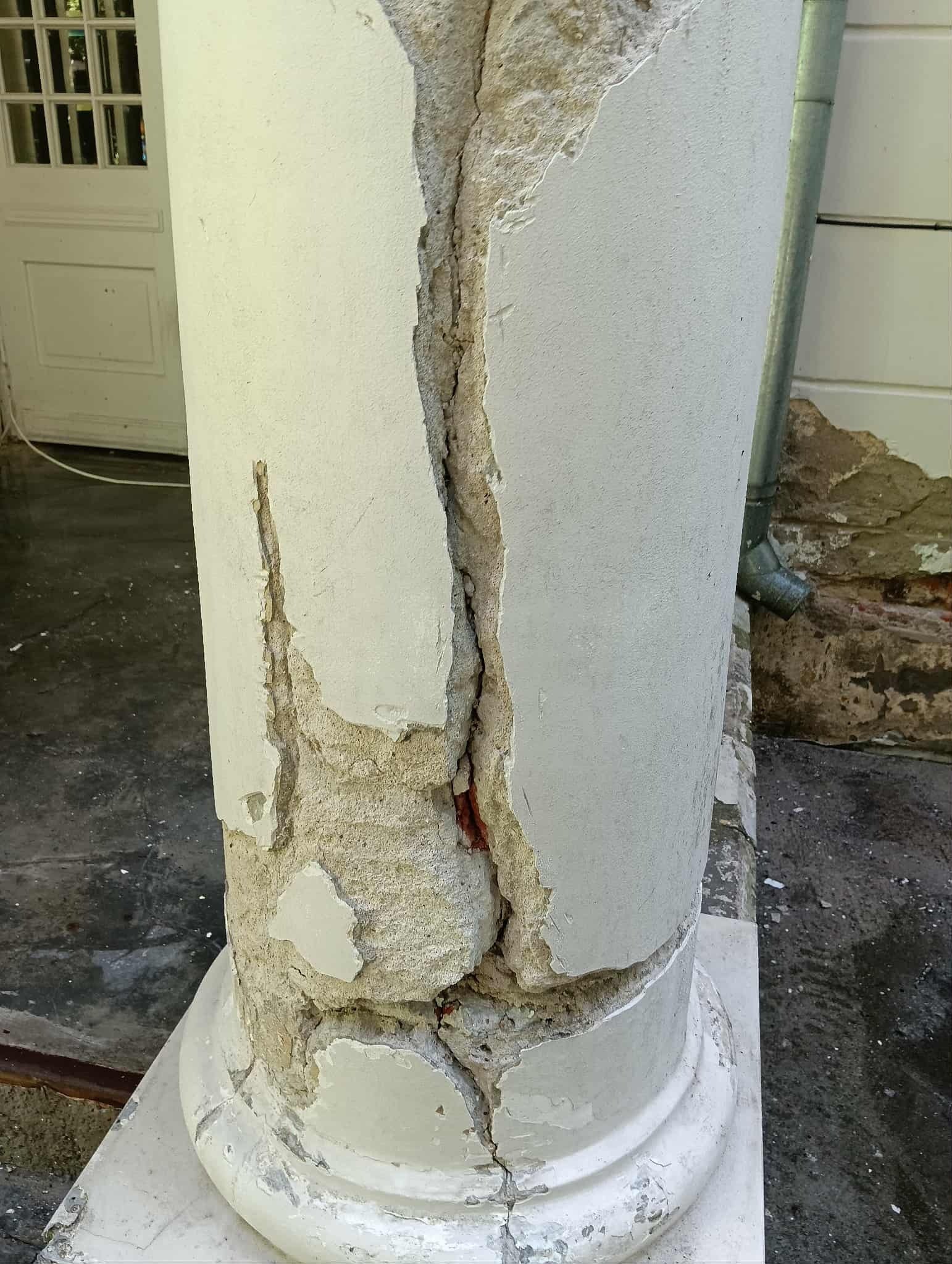 Zniszczona, popękana kolumna z odpadającym tynkiem. Widoczne ubytki i uszkodzenia struktury. Potrzeba pilnego remontu i renowacji.