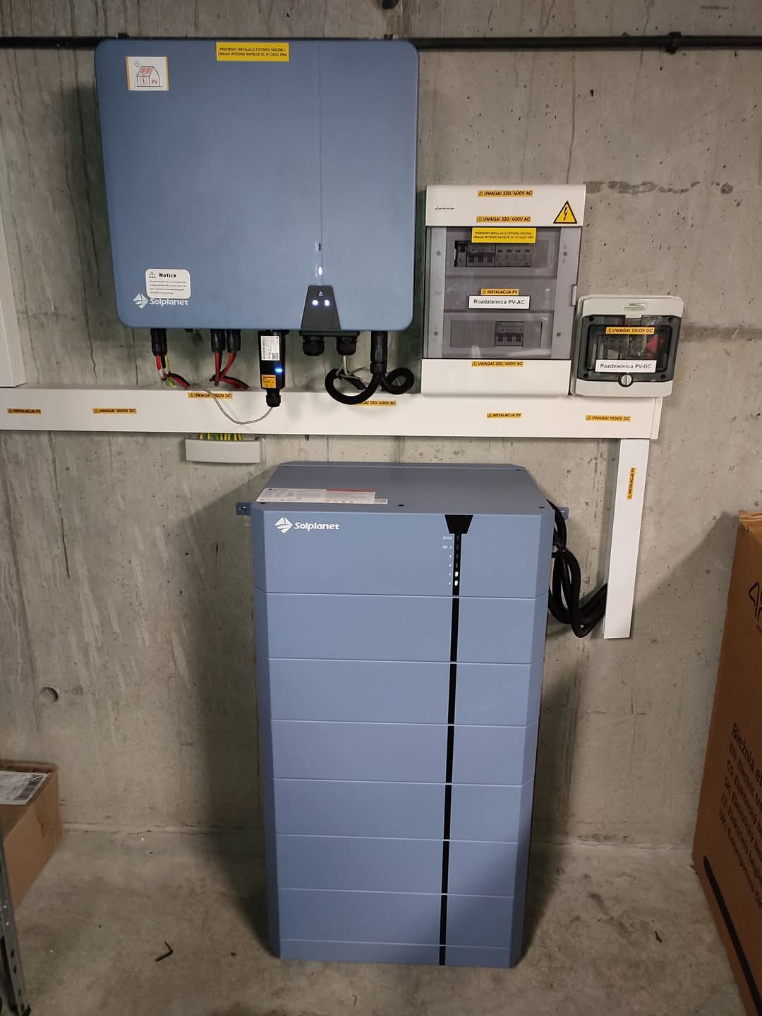Kompletna instalacja: falownik, rozdzielnice AC/DC i magazyn energii Solplanet na surowej ścianie. Widoczne okablowanie i oznaczenia napięć.