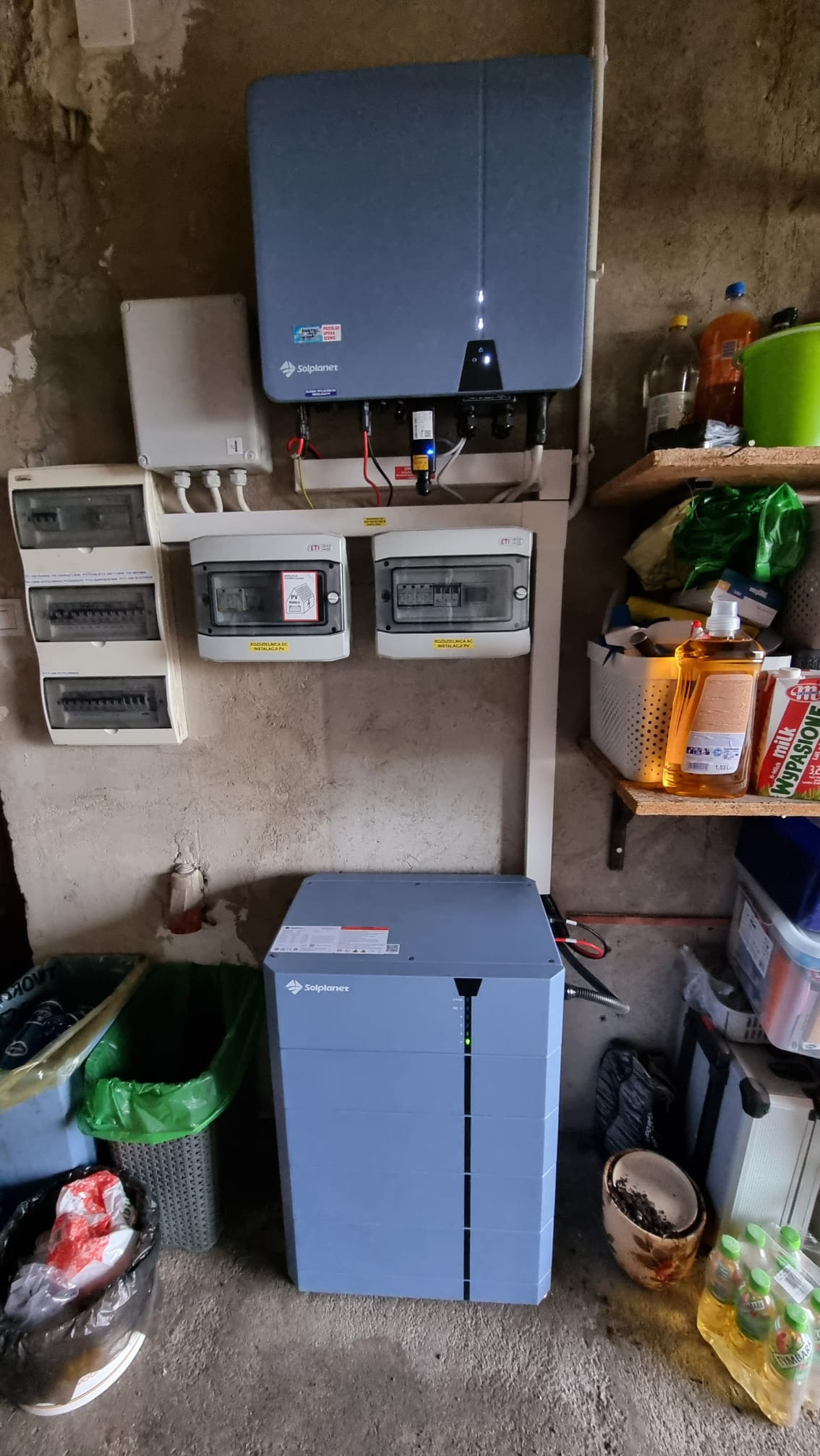 Instalacja magazynu energii Solplanet w pomieszczeniu gospodarczym. Widoczne rozdzielnice elektryczne, okablowanie i półki z różnymi przedmiotami.