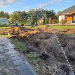 FILTOP Filip Bałdyga - Wykop pod system nawadniania w Łysem, widoczna instalacja zraszająca i przygotowany teren w pobliżu kostki brukowej.