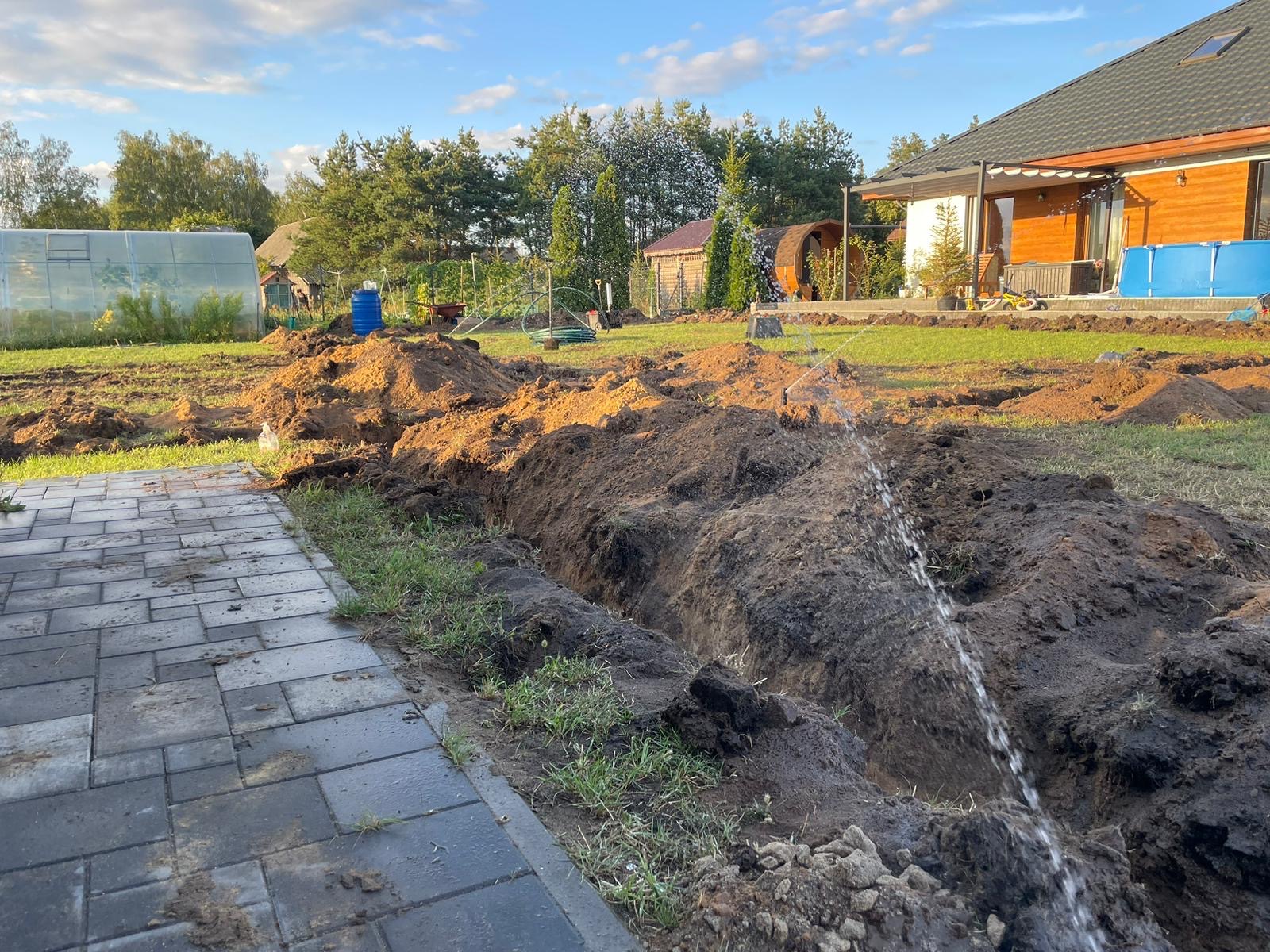 Wykop pod system nawadniania w Łysem, widoczna instalacja zraszająca i przygotowany teren w pobliżu kostki brukowej.