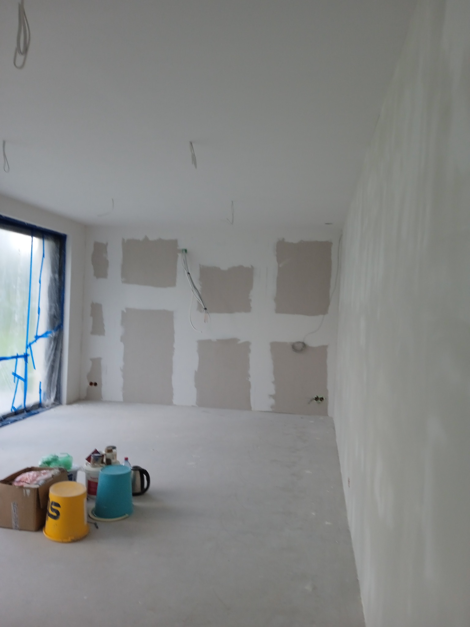 Pokój w trakcie szpachlowania ścian, widoczne puszki i narzędzia malarskie, okno zabezpieczone folią.