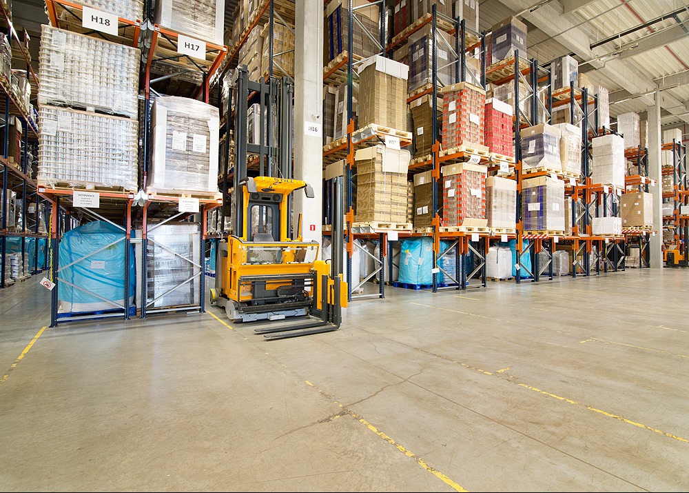 Wnętrze magazynu wysokiego składowania z wózkiem widłowym STILL, regały wypełnione paletami z towarem, oznaczenia H17 i H18 na regałach.