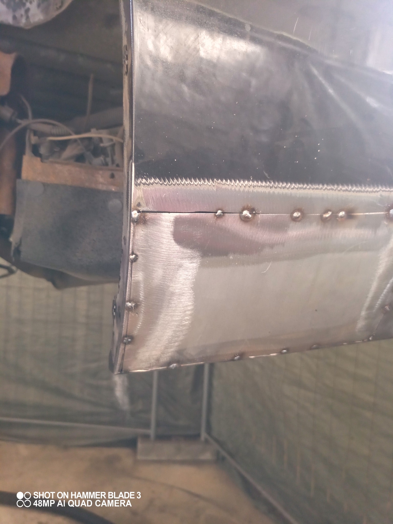 Metalowa konstrukcja połączona punktowymi spawami, widoczne ślady obróbki, w tle elementy pojazdu.