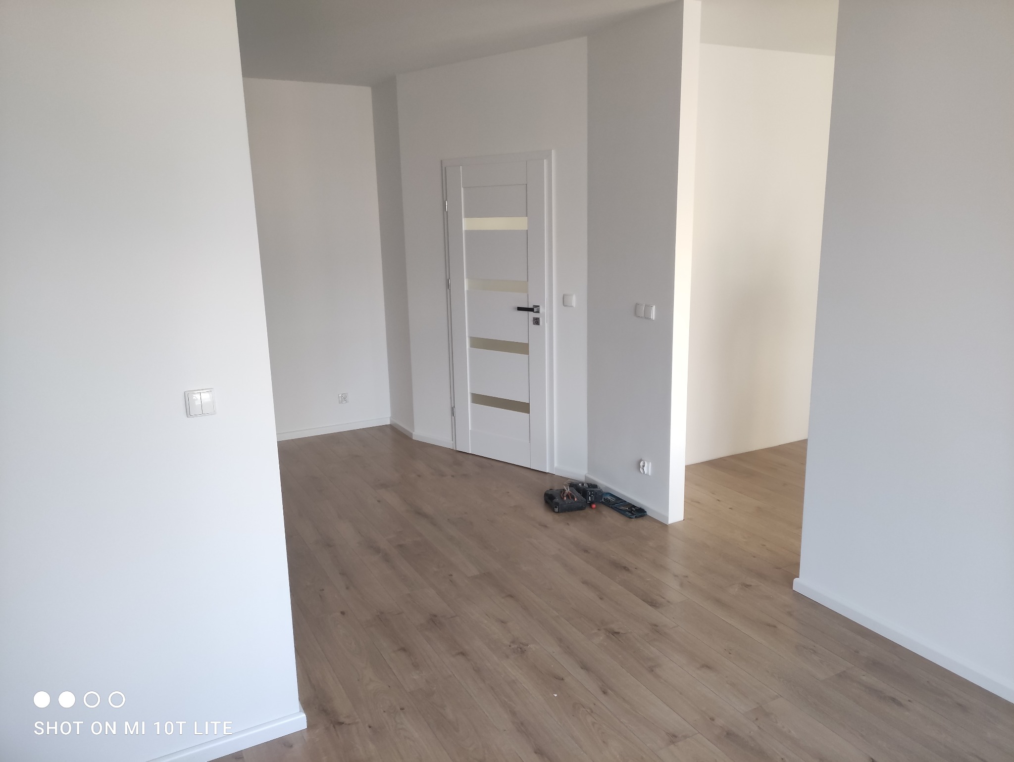 Puste, świeżo pomalowane na biało wnętrze z drewnianą podłogą, białe drzwi z przeszkleniami i narzędzia leżące na podłodze.