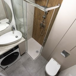 NIFU Jeremi Bombała - Nowoczesna łazienka z kabiną prysznicową wyłożoną drewnopodobnymi panelami, owalną umywalką nablatową, pralką pod blatem i szarą płytką podłogową.