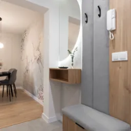 Nowoczesny przedpokój z okrągłym lustrem podświetlanym LED, tapetą w motywy roślinne i żurawi, drewnianą konsolą z półką, szarą tapicerowaną ławką i panelem ściennym z wieszakami oraz białym...