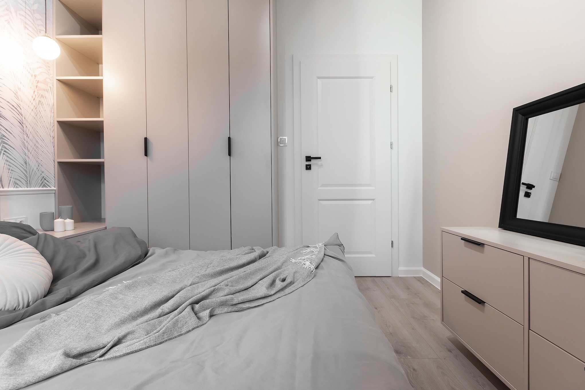 Jasnoszara sypialnia z łóżkiem, szafą na wymiar z otwartymi półkami, komodą i lustrem w czarnej ramie, minimalistyczny design