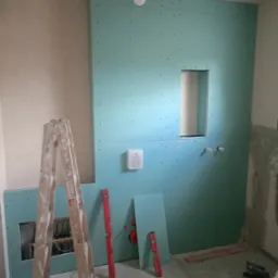 Montaż zielonej płyty karton gips w łazience w Pępowie, widoczne narzędzia, drabina i instalacja wodna w otworze.