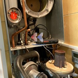 Termotechnika.Pro Rostysław Lisowski - Wnętrze pieca gazowego Viessmann z widocznymi elementami instalacji, w tym miedzianymi rurami i czarnym wentylatorem. Widoczny osprzęt Bosch.