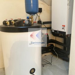 Termotechnika.Pro Rostysław Lisowski - Biały piec gazowy Viessmann z czarnymi rurami i zbiornikiem wyrównawczym w kotłowni. Widoczne przyłącza i elementy instalacji. Oświetlenie górne.