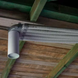 Cztery elastyczne, szare rury wentylacyjne zamontowane pod drewnianym stropem z zielonymi belkami nośnymi, widoczne z dołu.