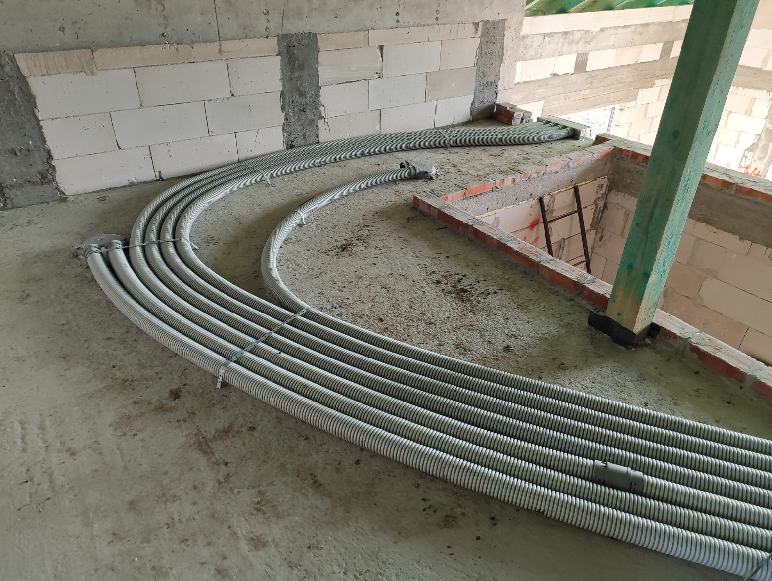 Rzędy karbowanych rur wentylacyjnych ułożone łukiem na surowym betonowym podłożu w trakcie instalacji w budynku w stanie surowym.