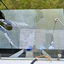 Tomasz Ejlak - Widok z góry na szklany dach patio podczas czyszczenia, z widocznymi drabinami, brudną powierzchnią, narzędziami i elementami otoczenia, takimi jak trawa i kostka brukowa.