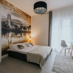 BaseElektric Artur Idasiak - Sypialnia z fototapetą przedstawiającą zabytkową architekturę nad rzeką, minimalistyczne meble i okrągłą lampę sufitową.