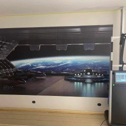 BaseElektric Artur Idasiak - Wielkoformatowa drukarka ścienna nanosi futurystyczny motyw stacji kosmicznej z widokiem na Ziemię, widoczne puste otwory na gniazdka elektryczne w ścianie.