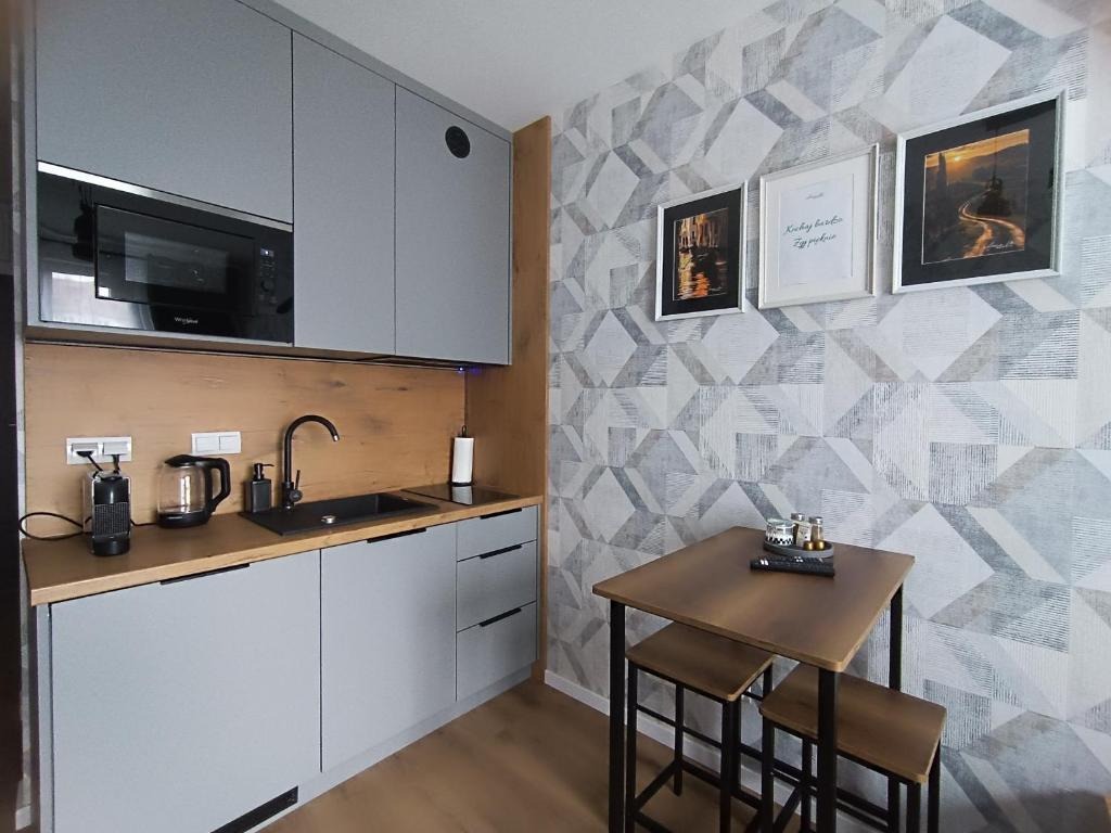 Nowoczesna, szara kuchnia z drewnianym blatem, czarną armaturą i geometryczną tapetą, uzupełniona małym stołem z krzesłami barowymi