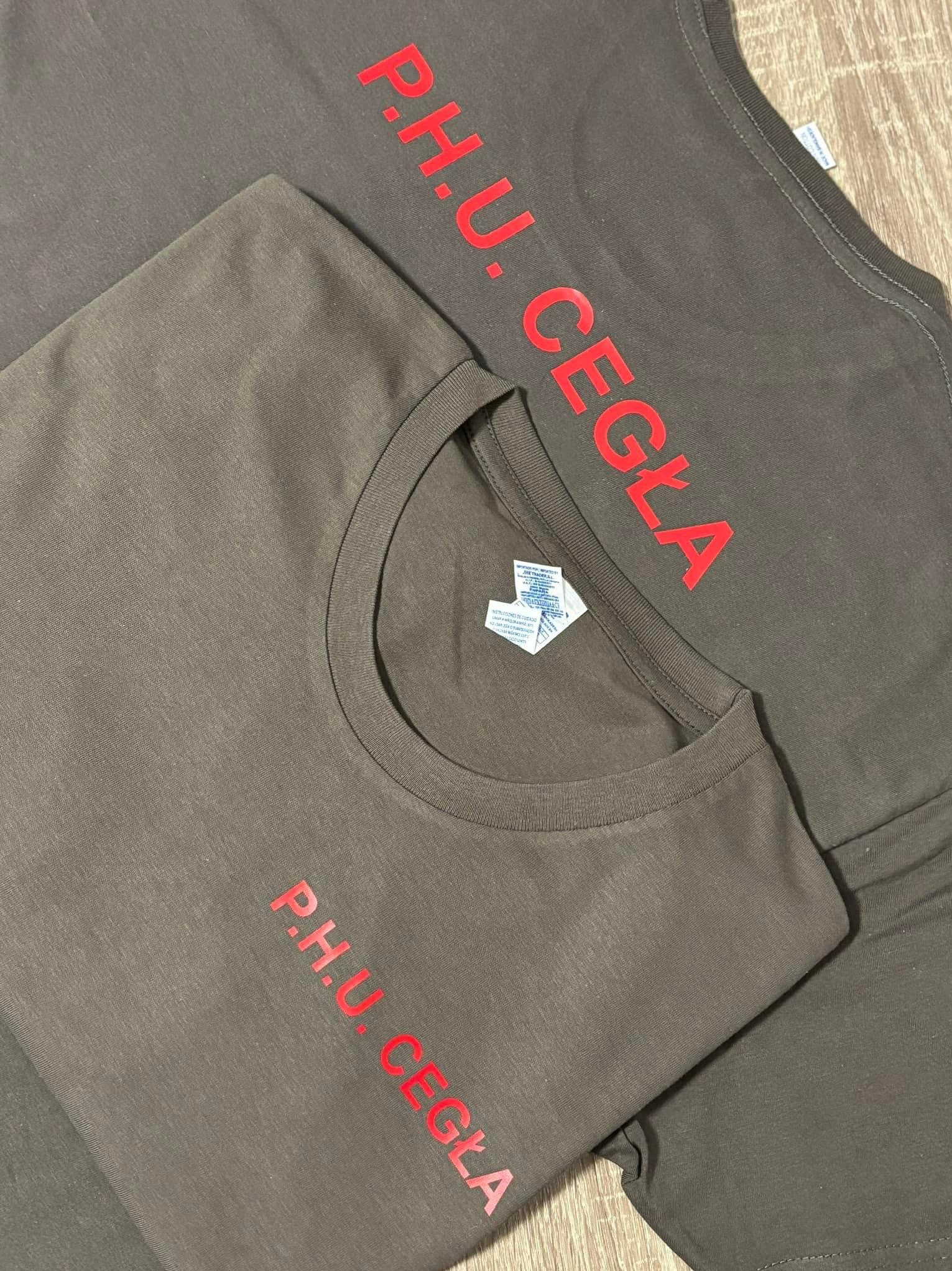 Dwie brązowe koszulki leżące na drewnianej podłodze, z czerwonym nadrukiem 'P.H.U. CEGŁA'.