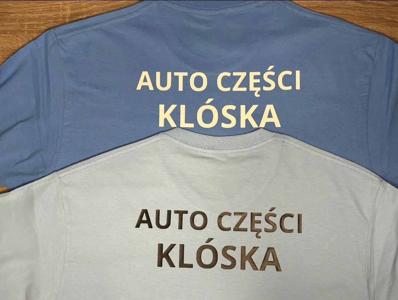 Dwa t-shirty, jeden błękitny, drugi jasnoniebieski, oba z nadrukiem 'AUTO CZĘŚCI KLÓSKA' w kolorze ciemnego złota, ułożone jeden na drugim.