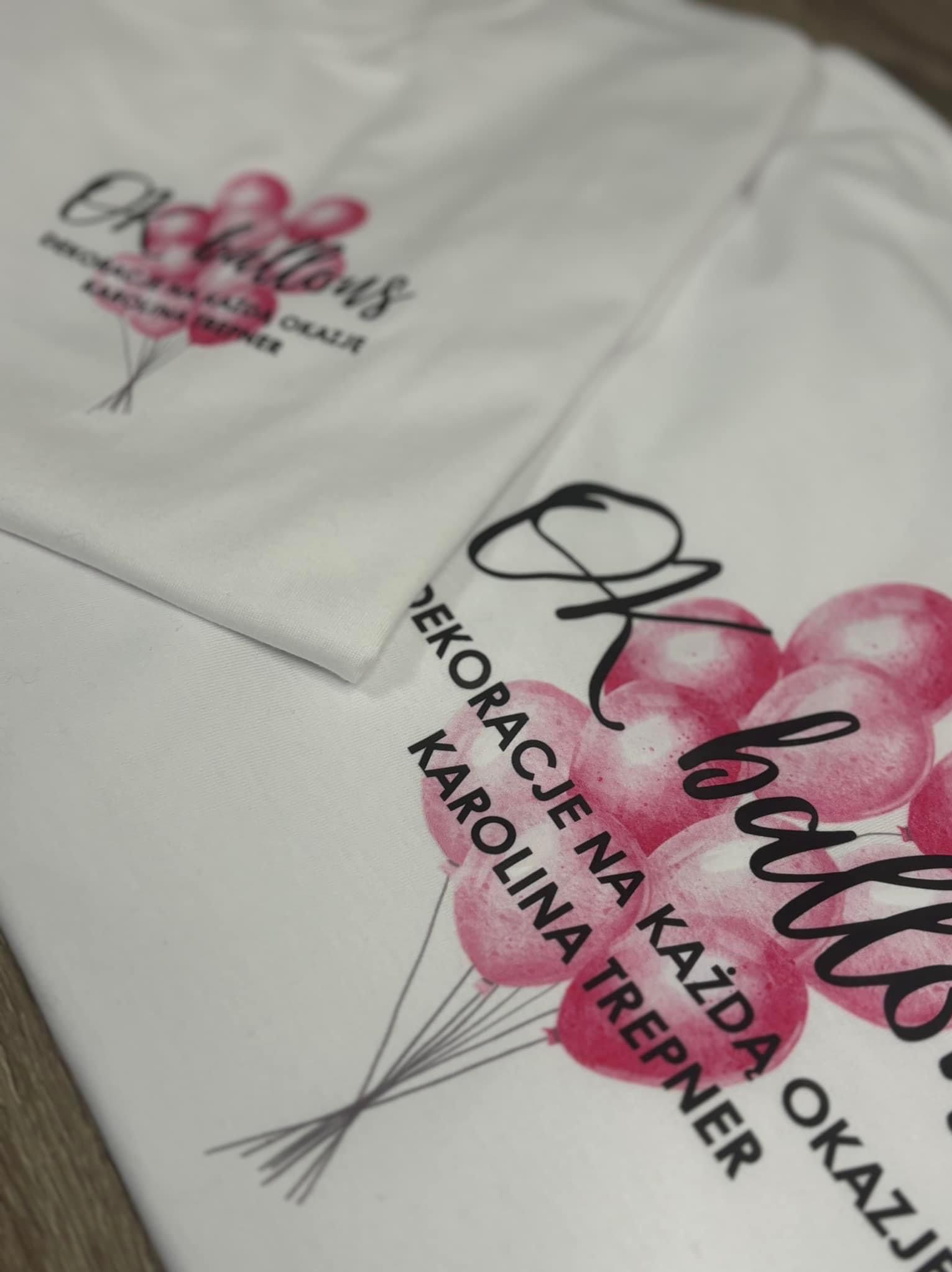 Dwa białe T-shirty z nadrukiem grafiki przedstawiającej różowe balony i napis 'Ok balloons DEKORACJE NA KAŻDĄ OKAZJĘ KAROLINA TREPNER'.