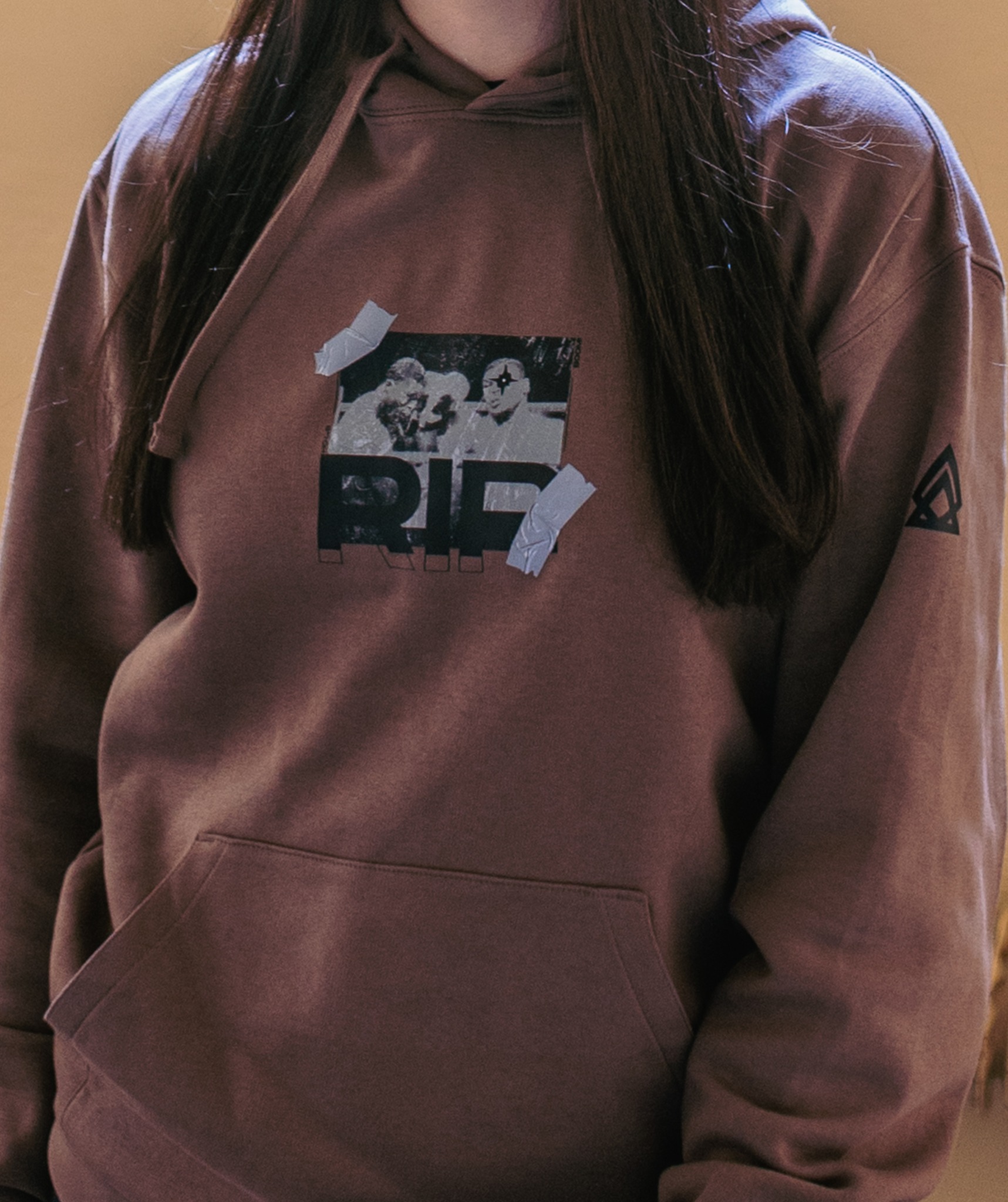 Brązowa bluza z kapturem, z nadrukiem czarno-białego zdjęcia przymocowanego taśmą klejącą, widoczny fragment sylwetki osoby noszącej.