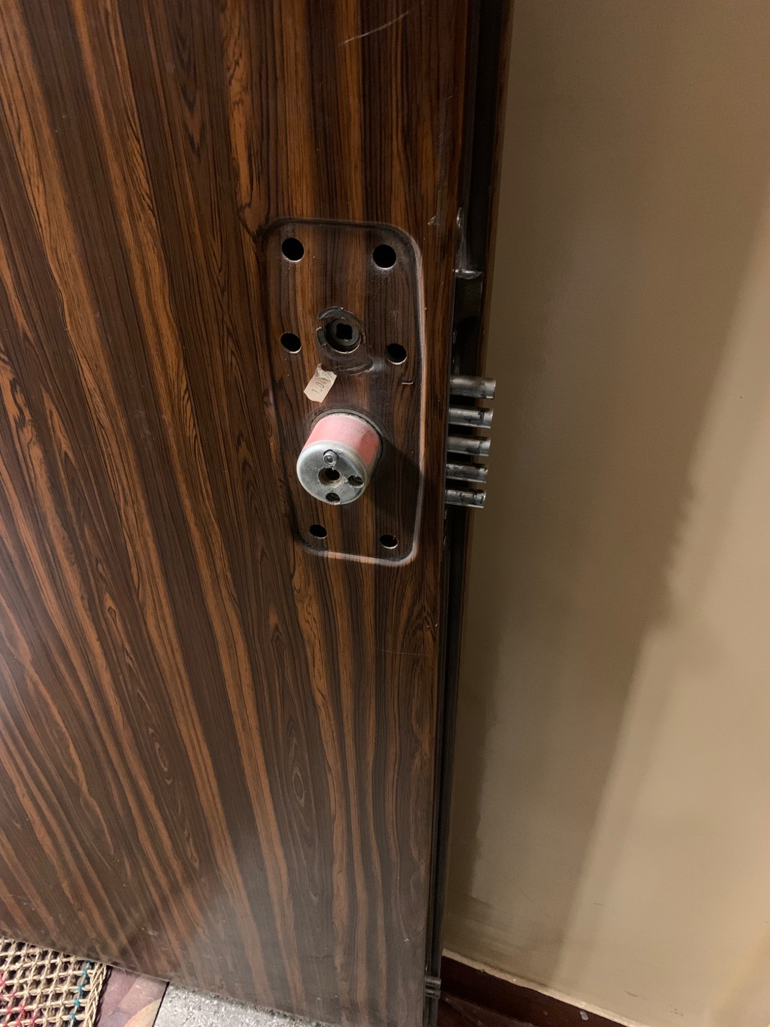 Brązowe drzwi wejściowe z widocznym zamkiem wielopunktowym i cylindrem z zabezpieczeniem, w trakcie montażu lub regulacji.