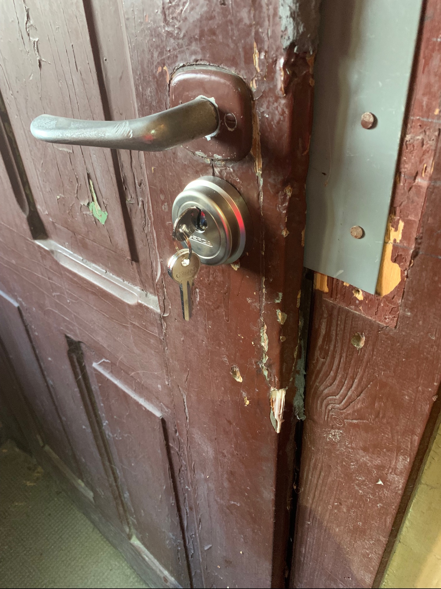 Stare drewniane drzwi wejściowe z widocznymi śladami zużycia, nowym zamkiem i kluczem w zamku.
