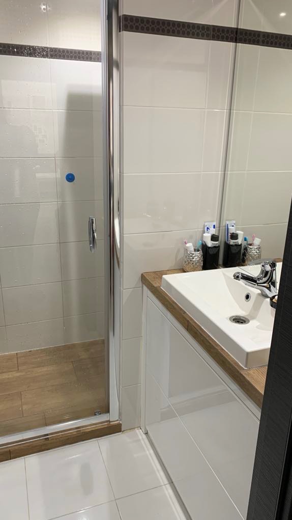 Nowoczesna łazienka z kabiną prysznicową ze szklanymi drzwiami, umywalką nablatową na szafce z drewnianym blatem i białymi płytkami z dekoracyjnym pasem.