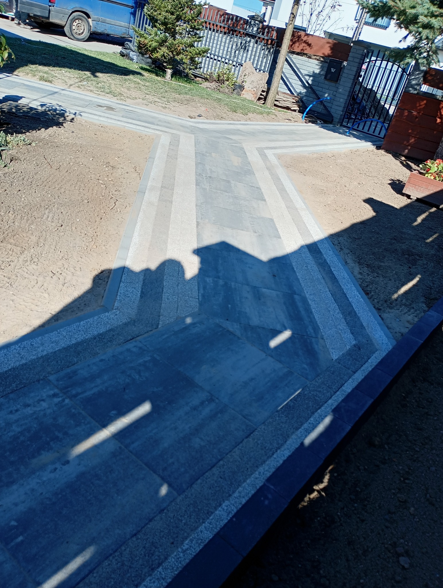 Nowo ułożona, dwukolorowa kostka brukowa prowadząca do furtki, z widocznymi schodkami i świeżo obsypaną ziemią po bokach.