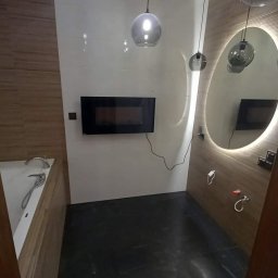 Wykończenia wnętrz od A do Z Tomasz Rzepka - Nowoczesna łazienka z czarną podłogą, białymi płytkami, drewnianymi akcentami, okrągłym lustrem z podświetleniem i wiszącymi lampami w kształcie kuli.