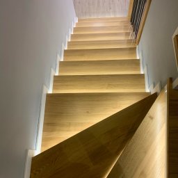 Usługi Stolarskie Paweł Jabłoński - Nowoczesne schody z drewna z podświetleniem LED, widok z góry, minimalistyczny design z białymi akcentami na szarym tle.