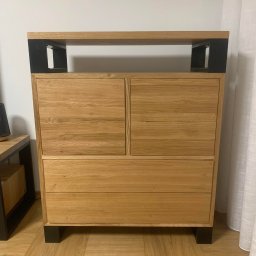 Usługi Stolarskie Paweł Jabłoński - Komoda z drewna dębowego z czterema szufladami i czarnymi metalowymi akcentami, stojąca na parkiecie w jasnym wnętrzu.