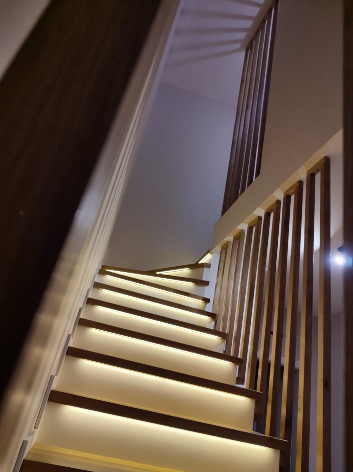 Nowoczesne schody z drewnianymi stopniami i podświetleniem LED, widok od dołu, minimalistyczna balustrada z pionowych listew.