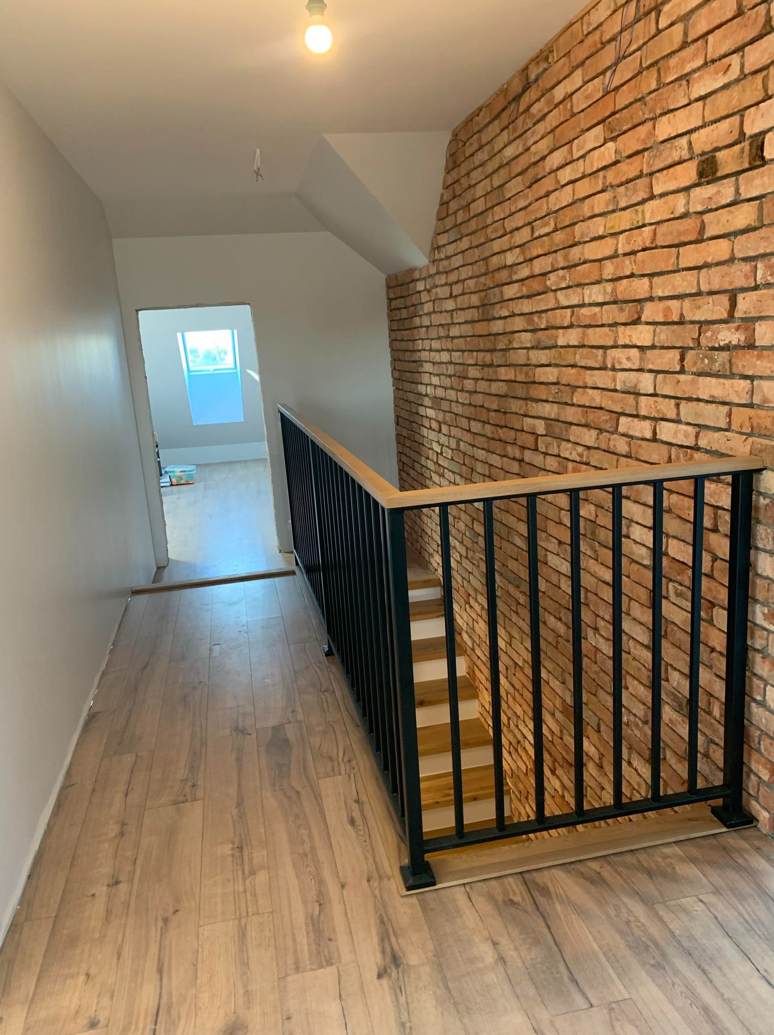 Nowoczesne schody z drewnianymi stopniami i czarną metalową balustradą, widok z góry na drewnianą podłogę, ściana z cegły w tle.