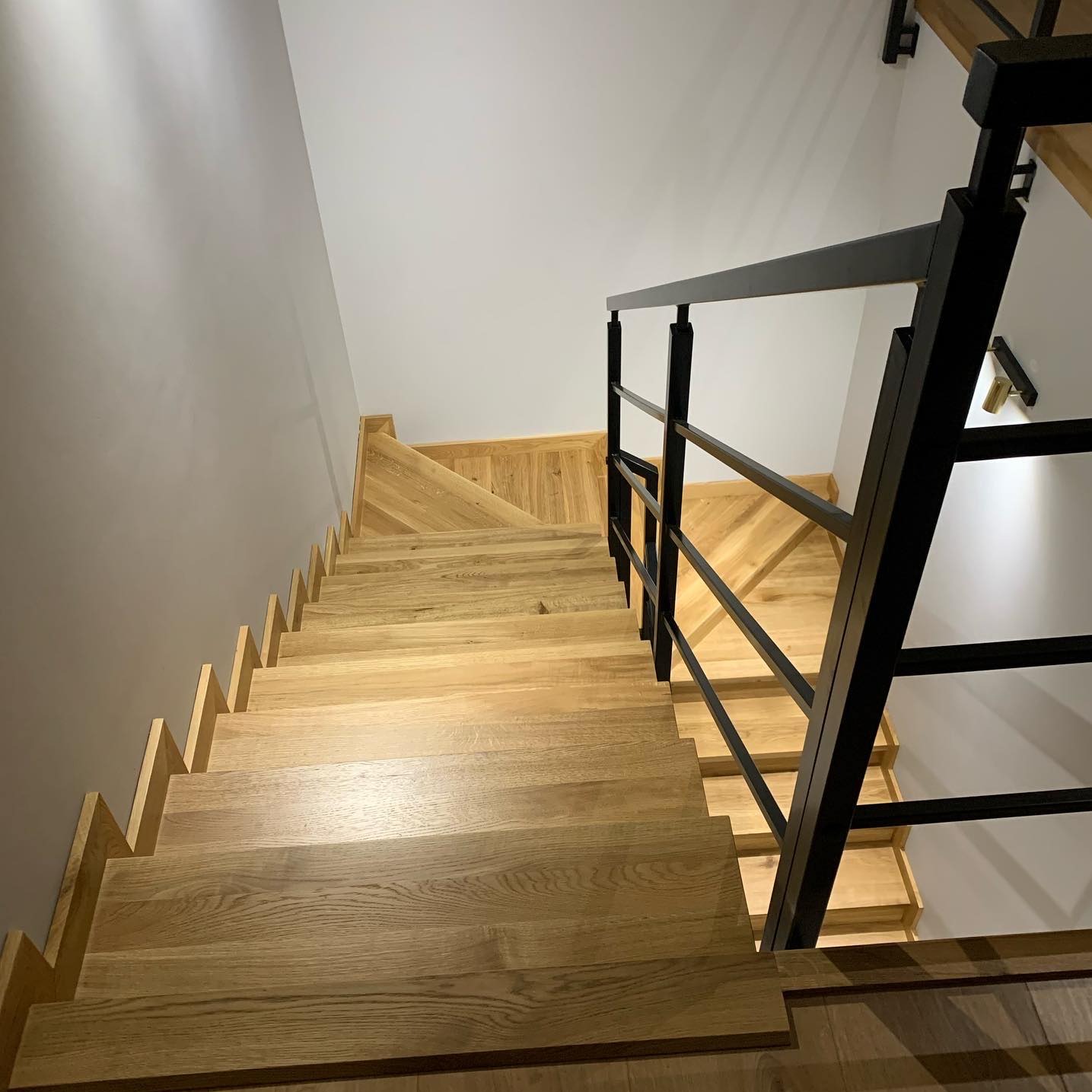 Drewniane schody z czarną, metalową balustradą widziane z góry, oświetlone ciepłym światłem, z widoczną fakturą drewna i minimalistycznym designem.